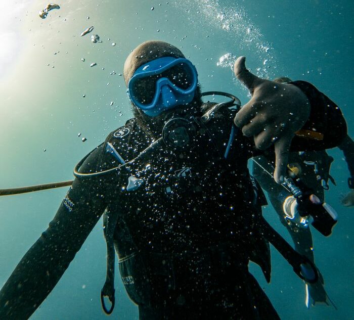 Scuba diver in Zanzibar's clear waters gives OK signal, surrounded by bubbles underwater.